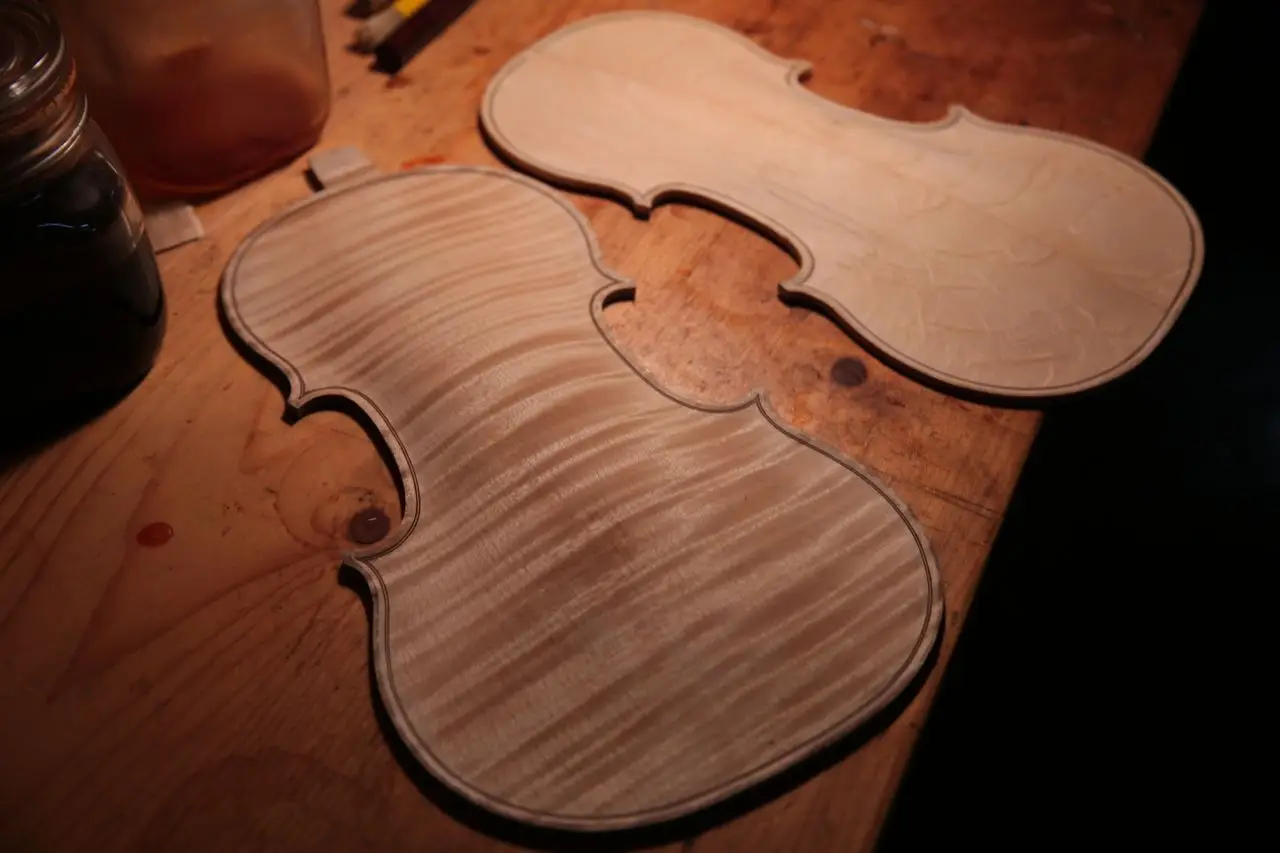 Close-up of wooden violin parts on a craftsman's workshop table.
